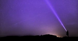 A man shining a flashlight into the sky that is edited to look bright purple.