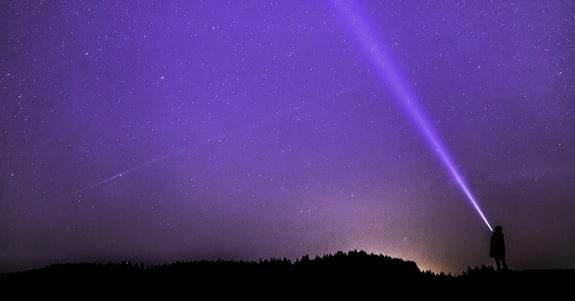 A man shining a flashlight into the sky that is edited to look bright purple.
