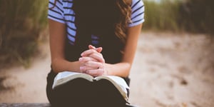Woman praying with hands folded over her bible. 