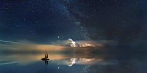 A sailboat on glassy water that is reflecting the stars above. 
