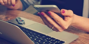 Woman working at her laptop while also looking at her phone. 