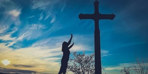 A woman worshipping in front of a cross.