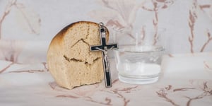 Bread, water, and a Crucifix on a marble table.