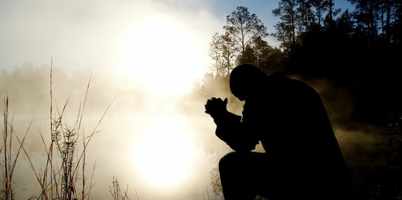 Man praying by a lake at sunrise. 
