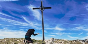 An individual praying before a cross on top of a mountain. 
