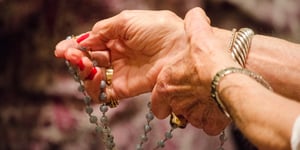 Elderly, female hands praying while holding rosary beads. 