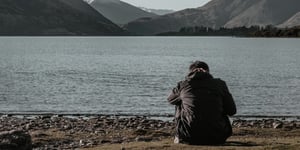 Man sad by the side of a lake. 