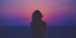 The silhouette of a woman that is illuminated by a pink and purple sunset. 
