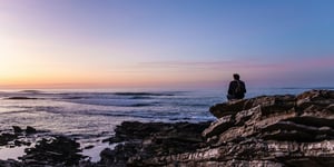 Man sitting on a big rock, overlooking the ocean, and maybe praying for a miracle.
