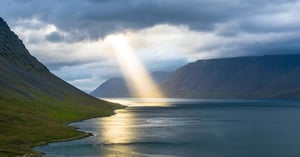 ray of sun shining down upon a body of water surrounded by mountains